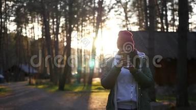 一个年轻的女孩正在拍摄一张照片，背景是一个森林村庄和一个美丽的日落。 慢动作，1920x1080，满
